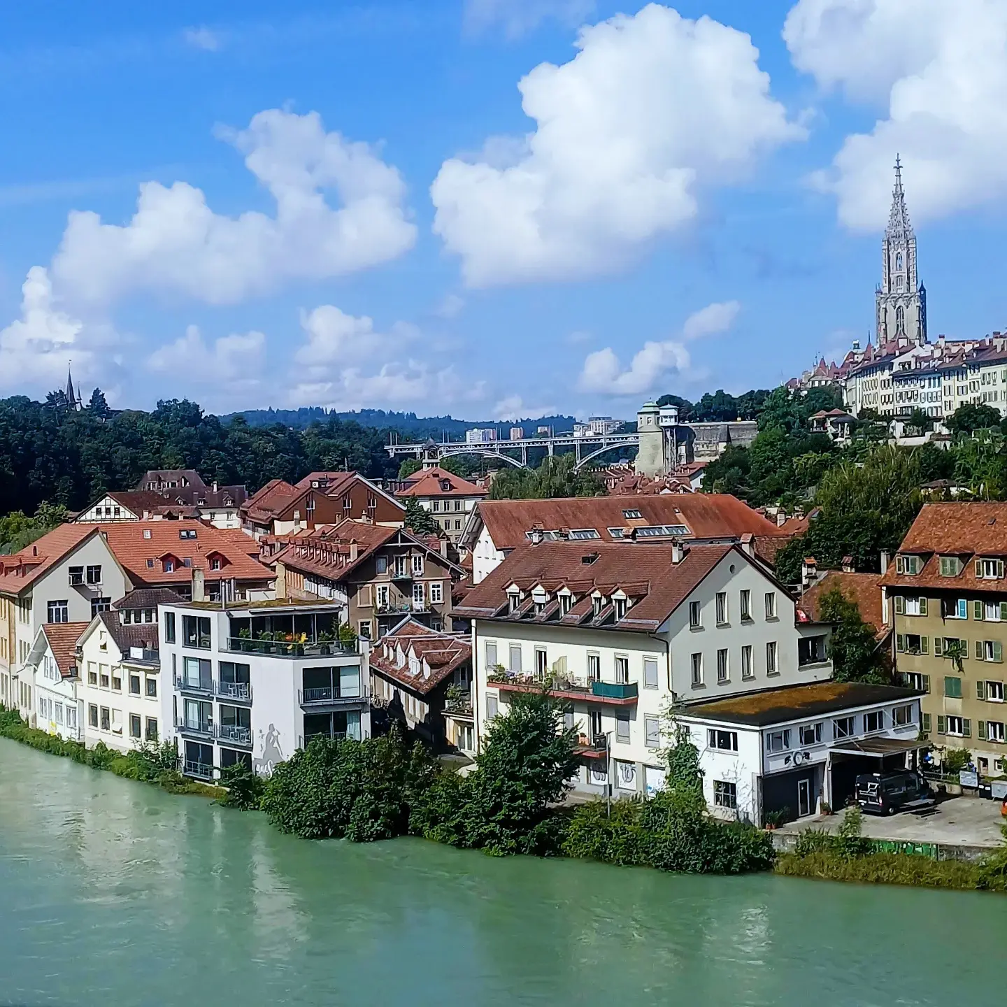 The turquoise Aare river below Bern's old town, red-roofed houses and the Münster spire under a sky of white clouds