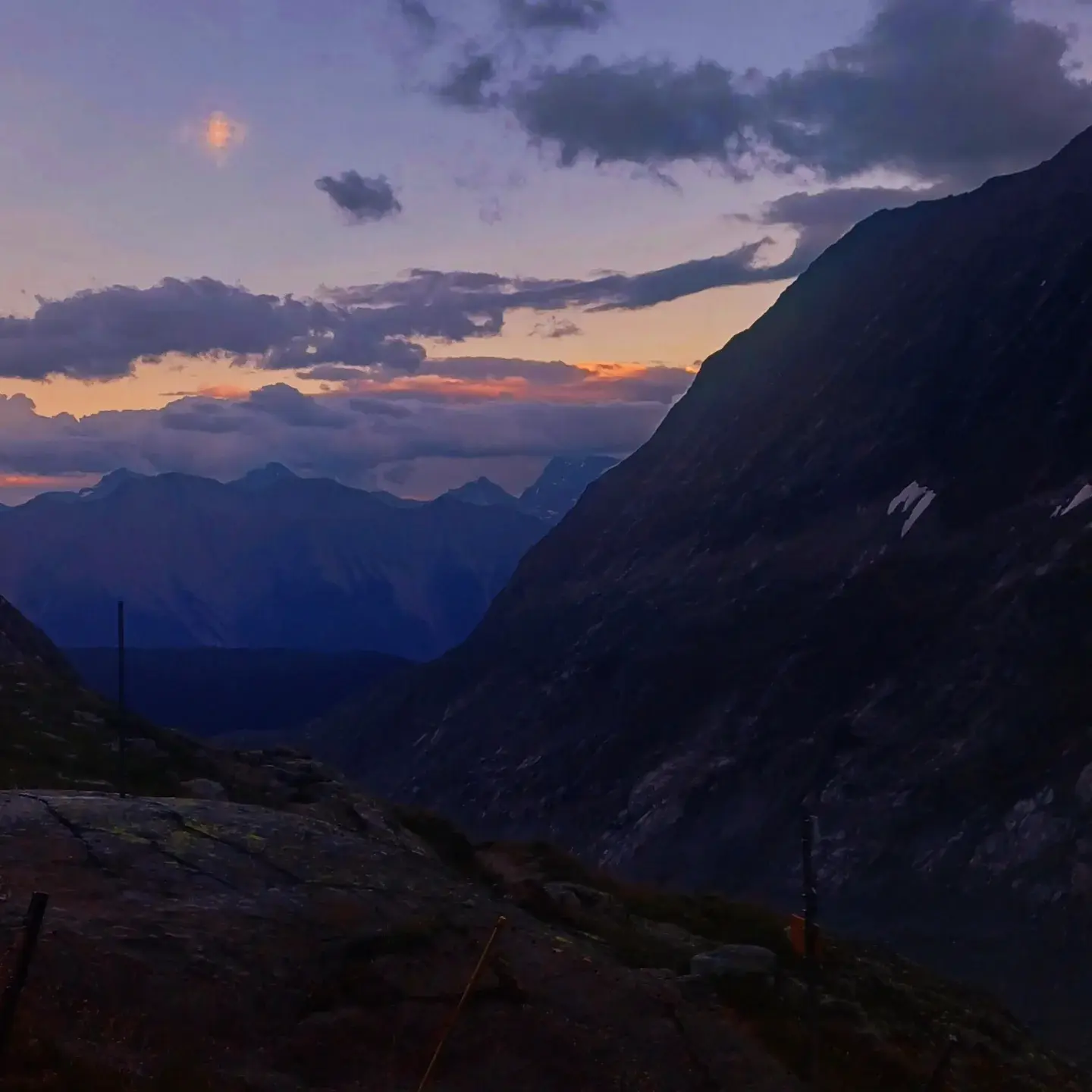 Dusk over an alpine valley, an orange and purple sky above dark mountain ridges