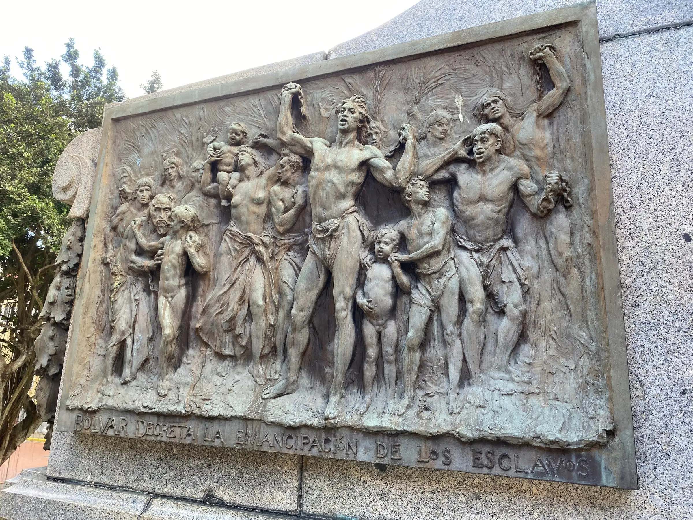 A bronze relief of freed people with raised arms, the inscription Bolívar decreta la emancipación de los esclavos beneath it