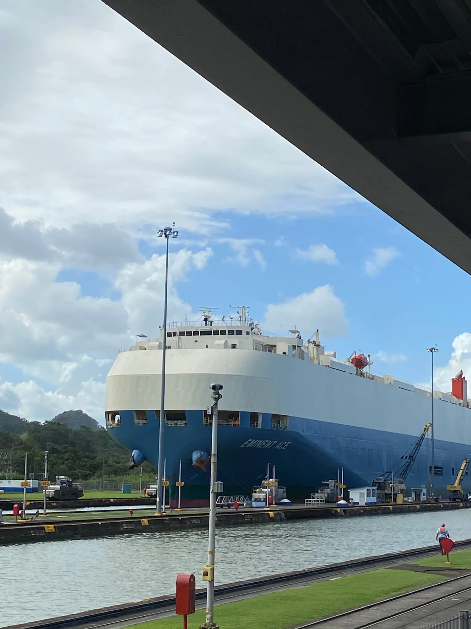 A large blue and white car carrier ship in a canal lock, lampposts and a red mailbox in the foreground