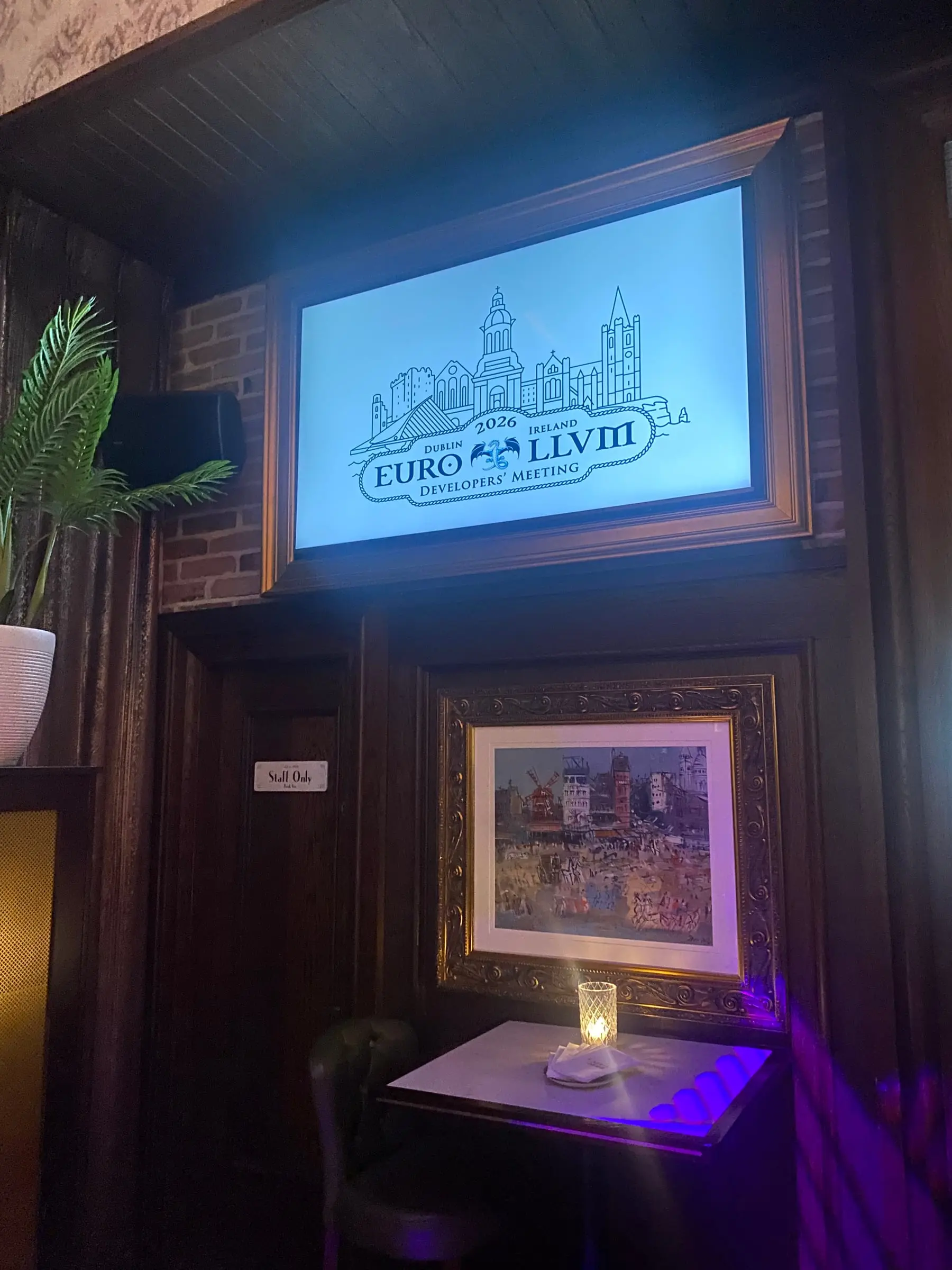 A lit sign reading EuroLLVM 2026 Developers' Meeting, Dublin, Ireland above a small table in a dark wood pub
